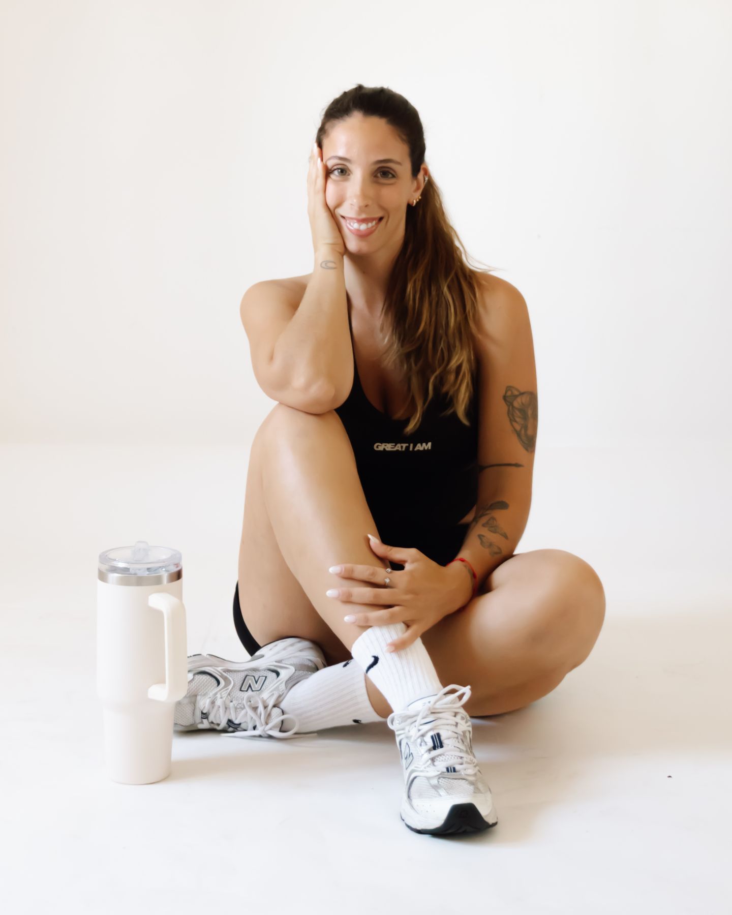 A coach sorri sentada no chão, com a mão no rosto.